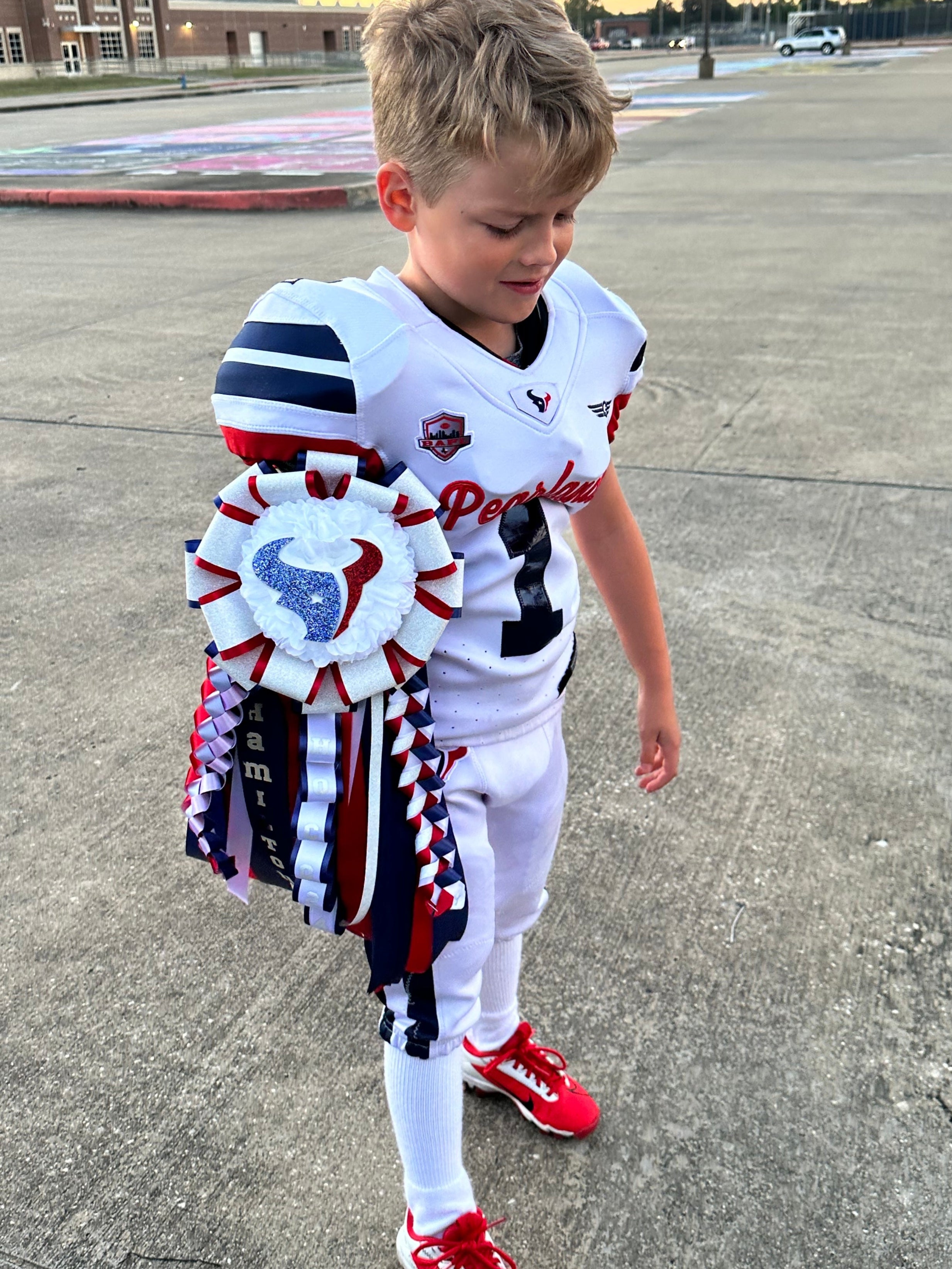 Young boy in sports uniform with a large ribbon standing on a concrete surface.