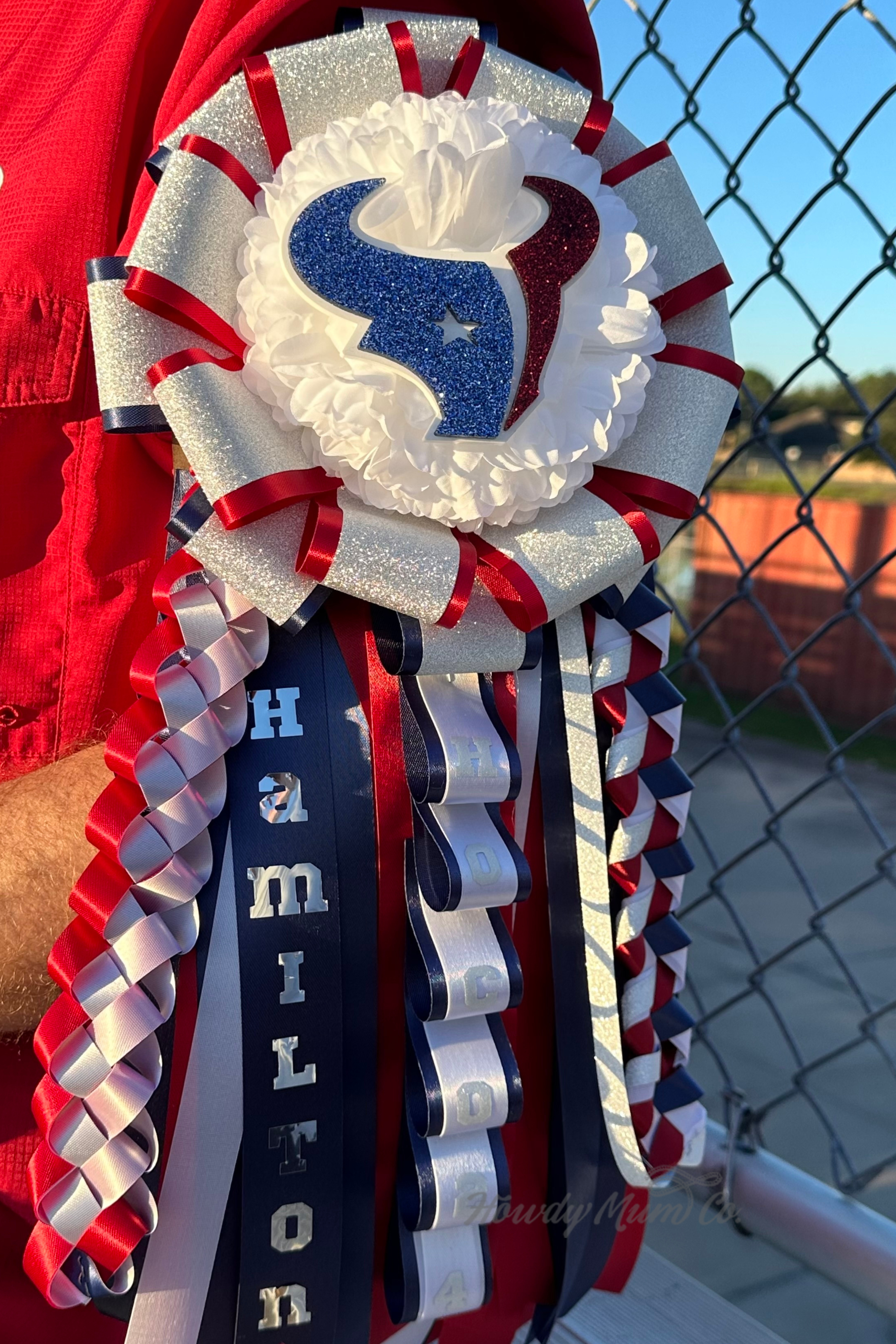 Decorative ribbon garter with Houston Texans logo and 'Hamilton' text, worn by a person in a red shirt.